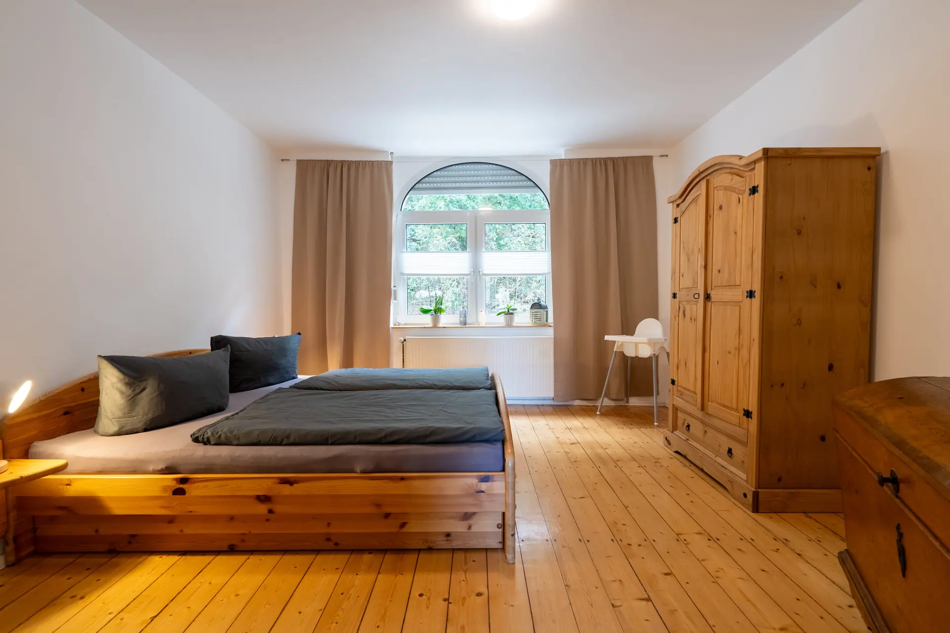 Schlafzimmer mit Doppelbett aus Holz, Kleiderschrank und Rundbogenfenster