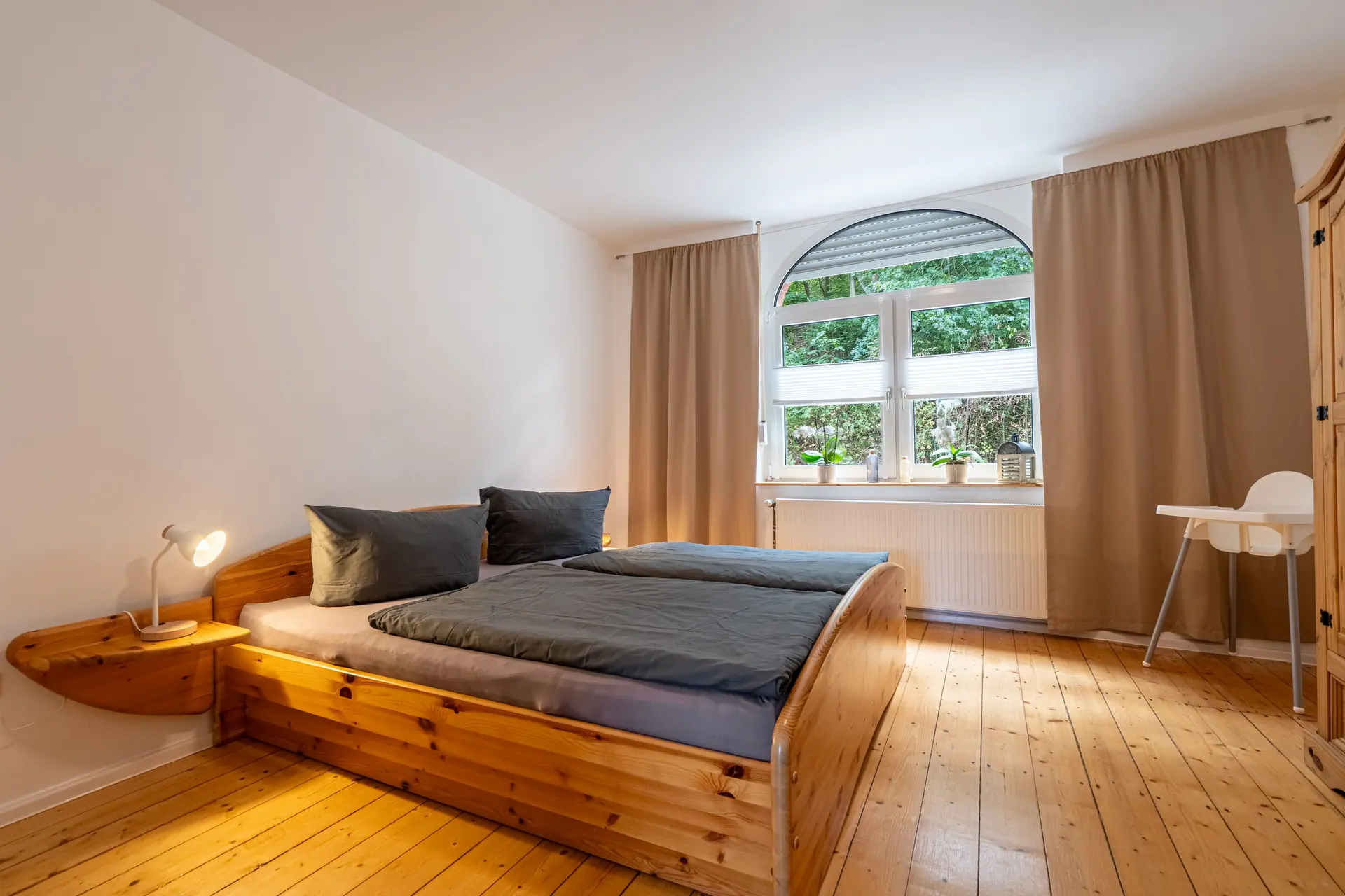Doppelbett vor einem Rundbogenfenster mit Vorhängen