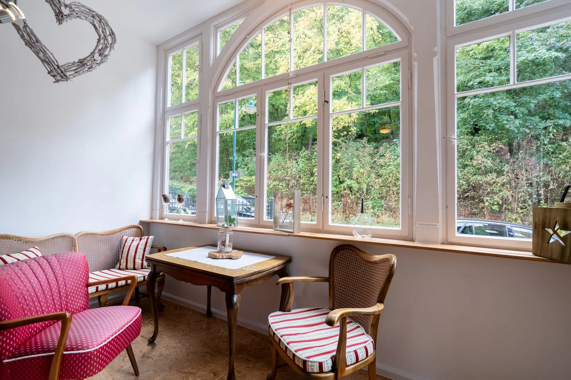 Veranda der Ferienwohnung mit großen Rundbogenfenstern, Sesseln und Blick ins Grün
