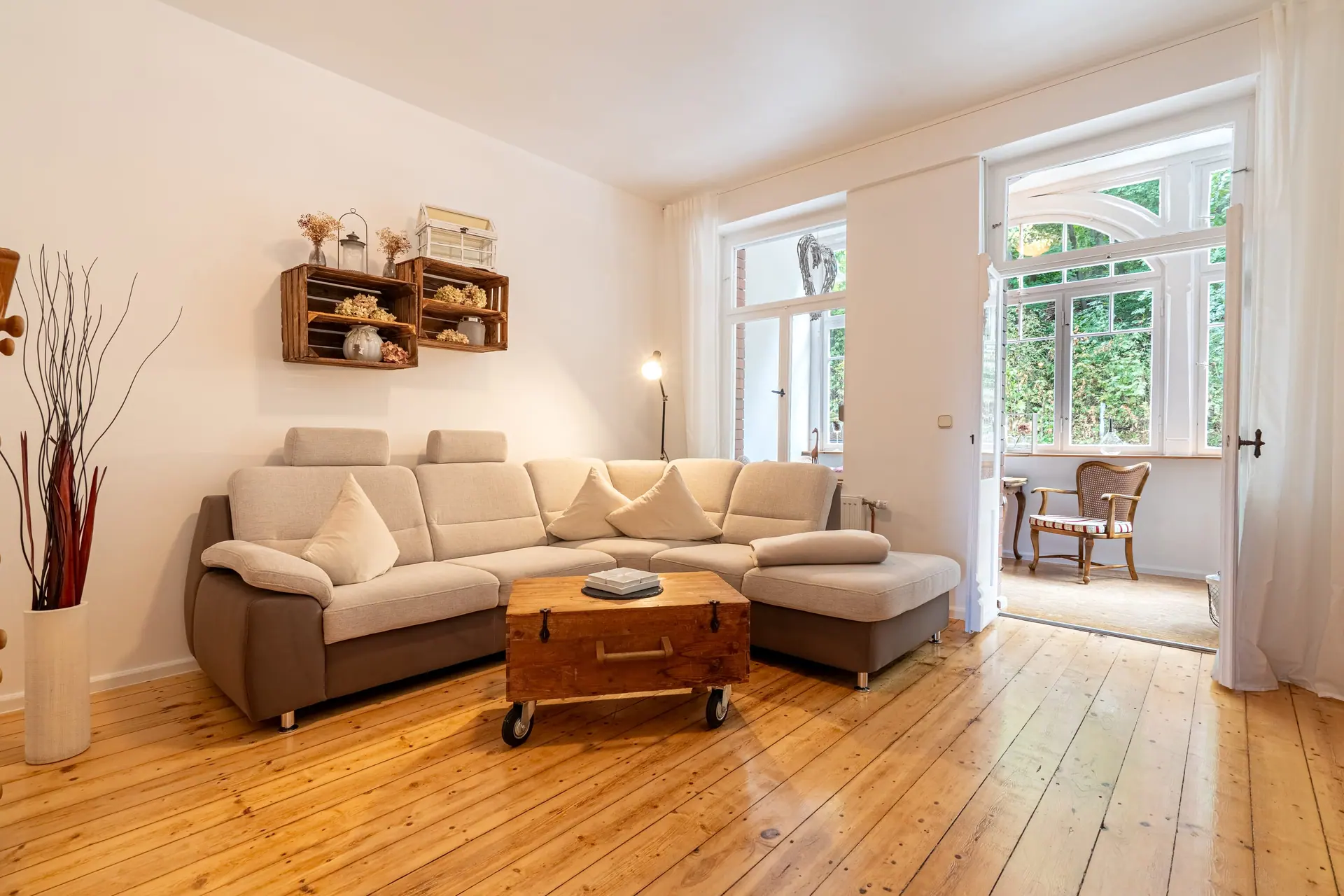 Wohnzimmer mit heller Sofaecke, Holzdielen und offener Tür zur Veranda